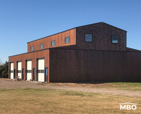 Barndominium with a rustic style on a flat lot with grass and trees