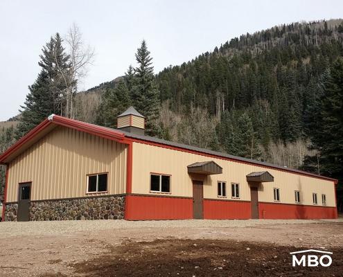 Agricultural Storage with red wainscot and tan walls with a red gable roof with a treed hill in the background